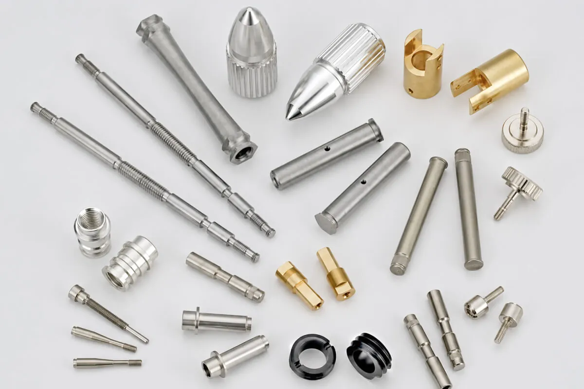 Custom CNC fasteners including stepped shafts, dowel pins, knurled thumb screws, collars, and brass bushings in stainless steel, aluminum, and brass